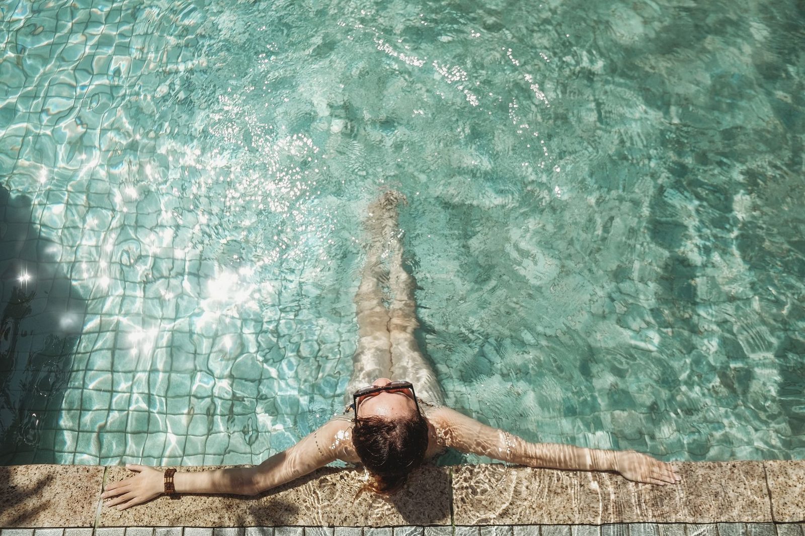 A woman enjoying a relaxing swim in a sunlit outdoor pool.