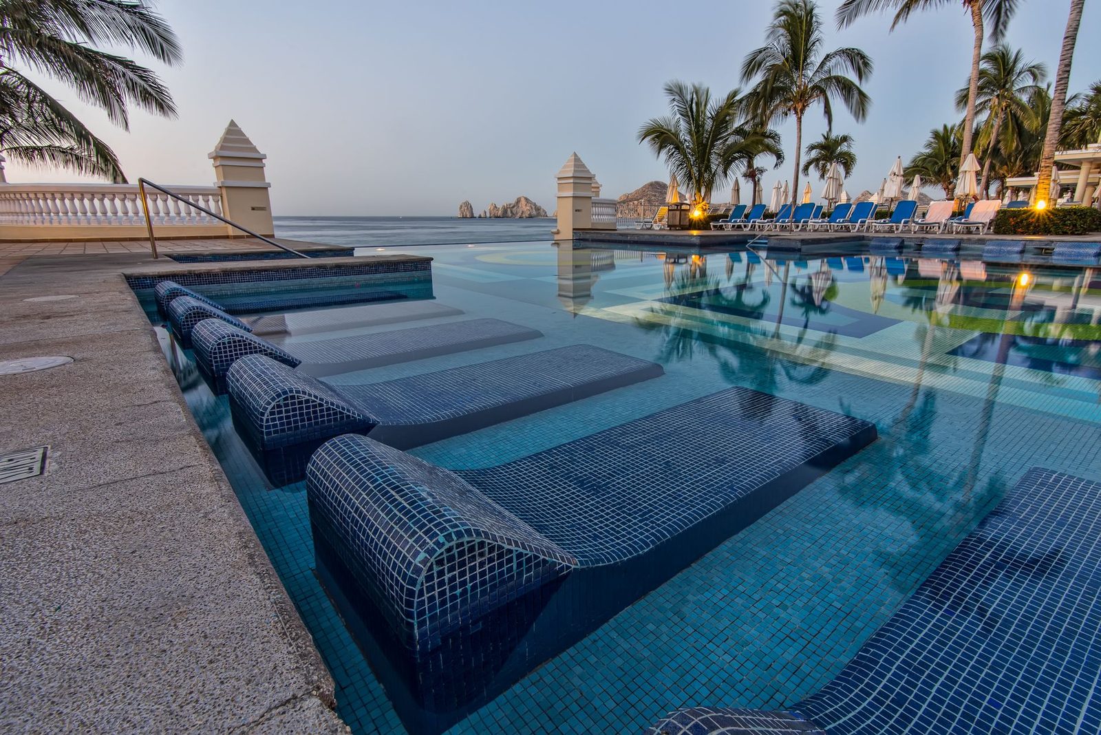 Serene poolside view overlooking the ocean with palm trees and lounge chairs in Cabo San Lucas, capturing