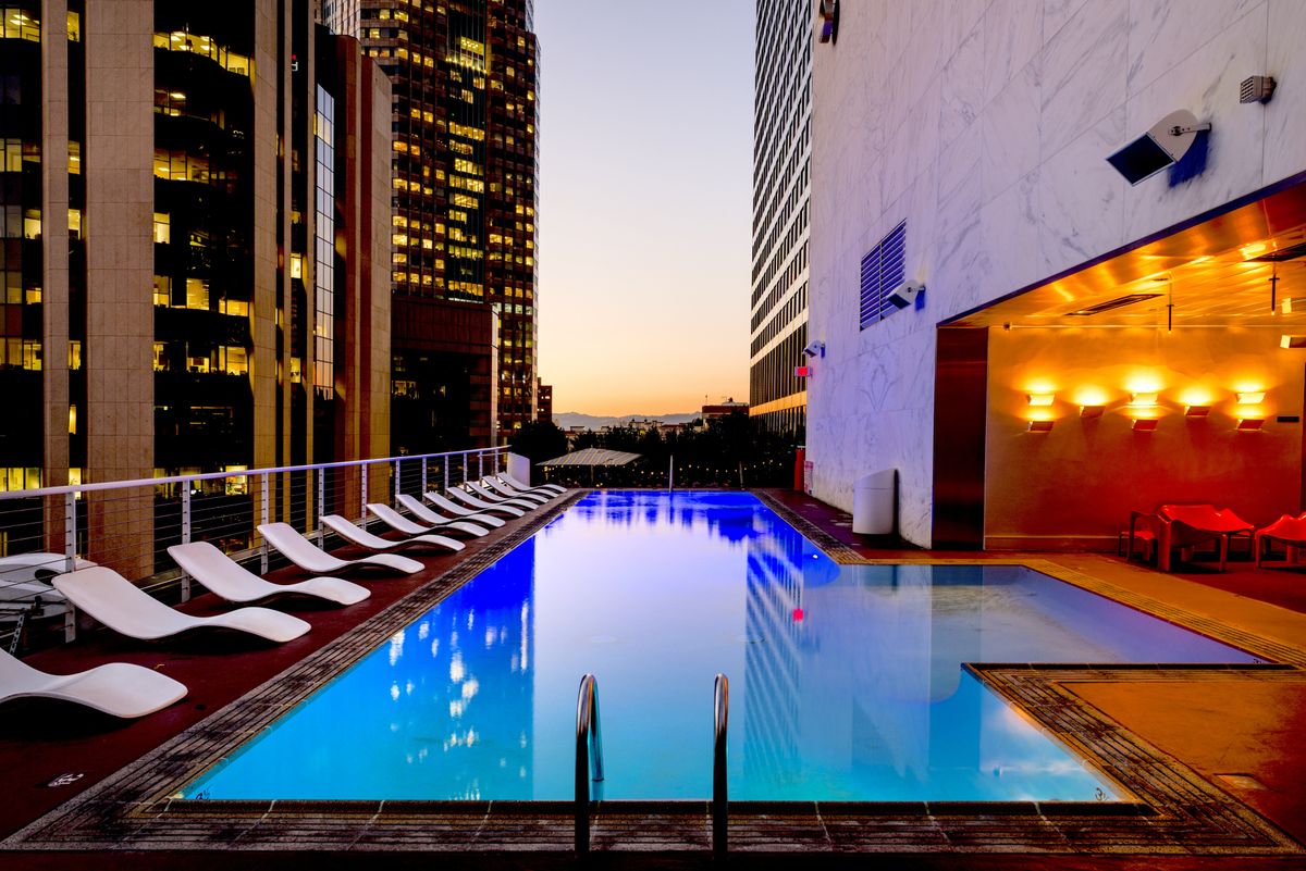 Rooftop swimming pool and lounge chairs between city buildings at sunset