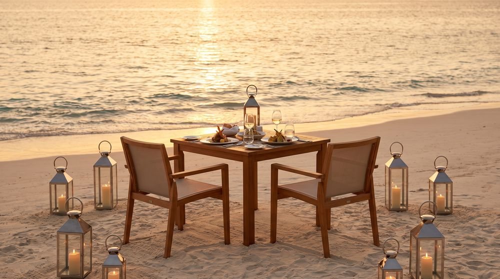 Two wooden chairs and a small table on a sandy beach with lanterns.