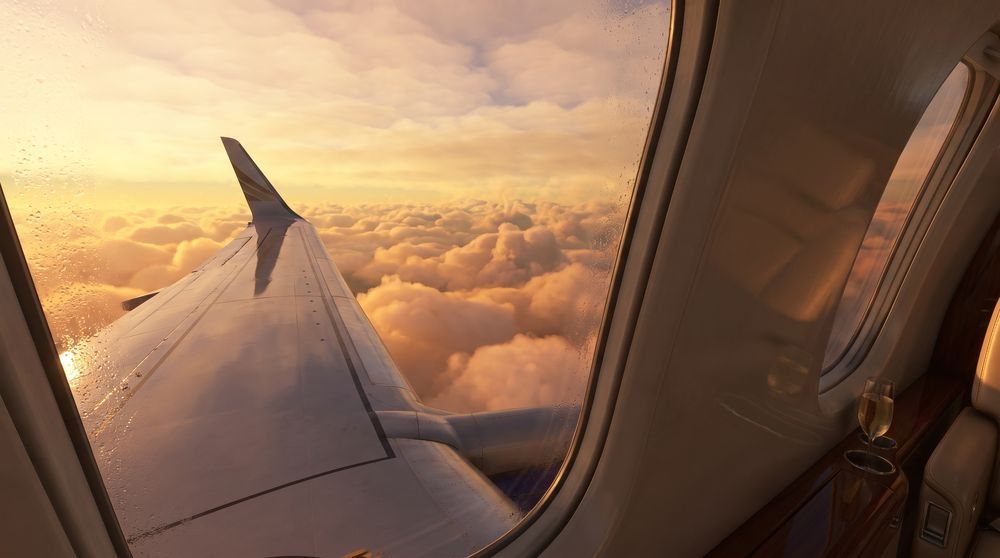 Airplane wing above clouds at sunset, with part of the cabin visible